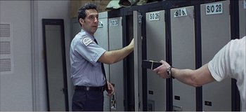 Movie still from “Fear X” (2003), directed by Nicolas Winding Refn – A security guard taking a card out of a locker; Medium shot, Over the shoulder angle