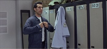 Movie still from “Fear X” (2003), directed by Nicolas Winding Refn – A man standing in front of lockers holding a shirt; Medium shot, Over the shoulder angle
