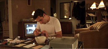 Movie still from “Fear X” (2003), directed by Nicolas Winding Refn – A man sitting at a table with a bowl of food; Medium shot, High angle