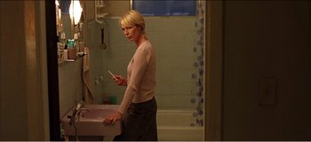 Movie still from “Fear X” (2003), directed by Nicolas Winding Refn – A woman standing in a bathroom next to a sink; Medium shot, High angle