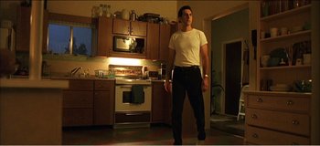 Movie still from “Fear X” (2003), directed by Nicolas Winding Refn – A man standing in a kitchen in front of a stove; Wide shot, Low angle