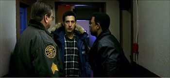 Movie still from “Fear X” (2003), directed by Nicolas Winding Refn – A group of men standing next to each other in a room; Medium shot, Over the shoulder angle