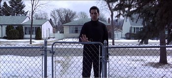 Movie still from “Fear X” (2003), directed by Nicolas Winding Refn – A man standing in front of a chain link fence; Medium shot, Low angle