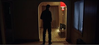 Movie still from “Fear X” (2003), directed by Nicolas Winding Refn – A man standing in a doorway looking into a living room; Wide shot, Low angle