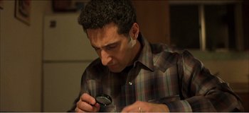 Movie still from “Fear X” (2003), directed by Nicolas Winding Refn – A man looking at something through a magnifying glass; Close Up shot, High angle