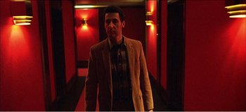 Movie still from “Fear X” (2003), directed by Nicolas Winding Refn – A man in a suit and tie standing in front of a red wall; Medium shot, Low angle