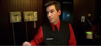 Movie still from “Fear X” (2003), directed by Nicolas Winding Refn – A man wearing a red shirt and black vest; Close Up shot, Over the shoulder angle