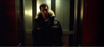 Movie still from “Fear X” (2003), directed by Nicolas Winding Refn – A man wearing a parka standing next to a wall; Medium shot, Low angle
