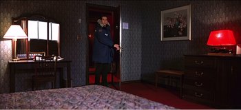 Movie still from “Fear X” (2003), directed by Nicolas Winding Refn – A man standing in front of an open door in a hotel room; Wide shot, High angle