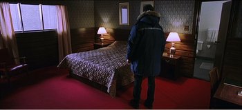 Movie still from “Fear X” (2003), directed by Nicolas Winding Refn – A man standing in front of a bed in a hotel room; Wide shot, High angle