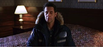 Movie still from “Fear X” (2003), directed by Nicolas Winding Refn – A man sitting on top of a bed wearing a jacket; Close Up shot, High angle