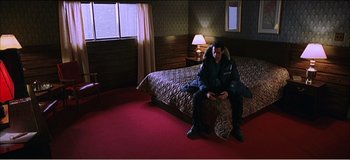Movie still from “Fear X” (2003), directed by Nicolas Winding Refn – A man sitting on a bed in front of a large bed; Wide shot, High angle