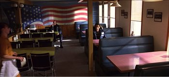 Movie still from “Fear X” (2003), directed by Nicolas Winding Refn – Two people sitting at a booth in a restaurant; Wide shot, High angle