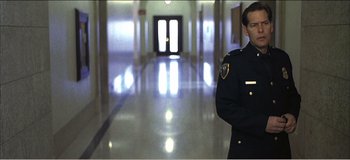 Movie still from “Fear X” (2003), directed by Nicolas Winding Refn – A man in a police uniform standing in a hallway; Medium shot, Low angle
