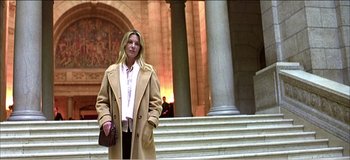 Movie still from “Fear X” (2003), directed by Nicolas Winding Refn – A woman standing in front of a building with a purse; Medium shot, Low angle