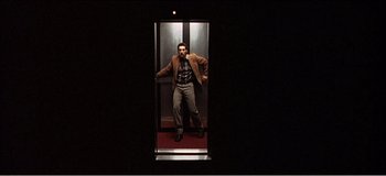 Movie still from “Fear X” (2003), directed by Nicolas Winding Refn – A man standing inside of an elevator in the dark; Wide shot, Low angle