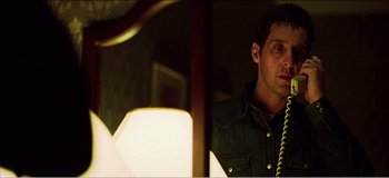 Movie still from “Fear X” (2003), directed by Nicolas Winding Refn – A man standing in front of a mirror holding a phone; Close Up shot, Low angle