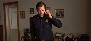 Movie still from “Fear X” (2003), directed by Nicolas Winding Refn – A police officer talking on a cell phone; Medium shot, Low angle