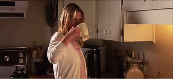 Movie still from “Fear X” (2003), directed by Nicolas Winding Refn – A woman drinking a cup of coffee in a kitchen; Medium shot, Over the shoulder angle