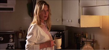 Movie still from “Fear X” (2003), directed by Nicolas Winding Refn – A woman holding a coffee mug in a kitchen; Close Up shot, Over the shoulder angle