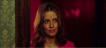 Movie still from “Fear X” (2003), directed by Nicolas Winding Refn – A woman in a pink shirt is smiling for the camera; Close Up shot, Over the shoulder angle