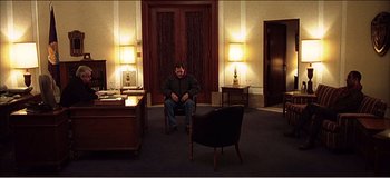 Movie still from “Fear X” (2003), directed by Nicolas Winding Refn – A man sitting on a chair in a room; Wide shot, High angle