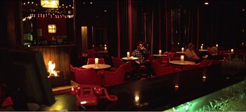 Movie still from “Fear X” (2003), directed by Nicolas Winding Refn – A man sitting at a table in front of candles; Wide shot, High angle