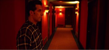 Movie still from “Fear X” (2003), directed by Nicolas Winding Refn – A man standing in a hallway with red walls; Medium shot, Low angle