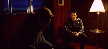 Movie still from “Fear X” (2003), directed by Nicolas Winding Refn – Two men are sitting in a dark room; Medium shot, High angle