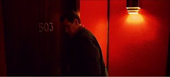 Movie still from “Fear X” (2003), directed by Nicolas Winding Refn – A man standing in front of a red door; Close Up shot, High angle