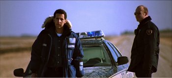 Movie still from “Fear X” (2003), directed by Nicolas Winding Refn – A man standing in front of a police car; Medium shot, Low angle