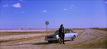 Movie still from “Fear X” (2003), directed by Nicolas Winding Refn – A man standing next to a car on the side of the road; Extreme Wide shot, Low angle