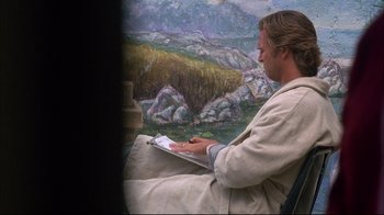 Movie still from “Fearless” (1993), directed by Peter Weir – A man sitting in front of a painting while holding a pencil; Medium shot, Low angle