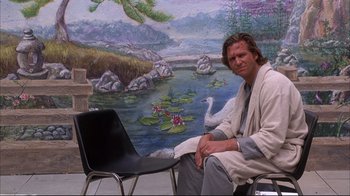 Movie still from “Fearless” (1993), directed by Peter Weir – A man sitting in front of a painting of a swan; Medium shot, Low angle