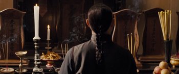 Movie still from “Fearless” (2006), directed by Ronny Yu – A person with a long braid is sitting in front of a table; Close Up shot, Over the shoulder angle