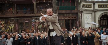 Movie still from “Fearless” (2006), directed by Ronny Yu – A man with a shaved head and a bald head in front of a group of people; Medium shot, Low angle