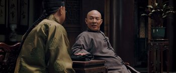 Movie still from “Fearless” (2006), directed by Ronny Yu – A man sitting on a chair talking to another man; Medium shot, Over the shoulder angle