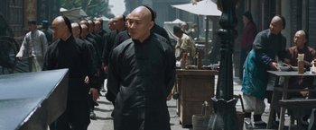 Movie still from “Fearless” (2006), directed by Ronny Yu – A man with a shaved head is walking down the street; Medium shot, Over the shoulder angle