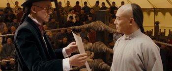 Movie still from “Fearless” (2006), directed by Ronny Yu – A man in a boxing ring holding a sheet of paper in front of a crowd of people; Medium shot, Over the shoulder angle