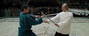 Movie still from “Fearless” (2006), directed by Ronny Yu – Two men are holding swords in front of an audience; Medium shot, High angle