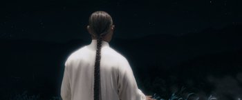 Movie still from “Fearless” (2006), directed by Ronny Yu – A person with a long braid standing in front of a night sky; Medium shot, Low angle