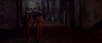Movie still from “Fellini Satyricon” (1969), directed by Federico Fellini – A couple of people standing next to each other in front of a statue; Extreme Wide shot, Over the shoulder angle