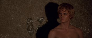 Movie still from “Fellini Satyricon” (1969), directed by Federico Fellini – A young man standing in front of a wall; Close Up shot, Over the shoulder angle