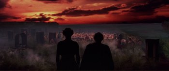 Movie still from “Fellini Satyricon” (1969), directed by Federico Fellini – Two people standing in front of a crowd at sunset; Extreme Wide shot, Over the shoulder angle