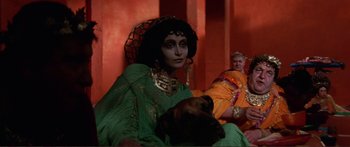 Movie still from “Fellini Satyricon” (1969), directed by Federico Fellini – A woman dressed as a witch sitting next to a dog; Medium shot, Over the shoulder angle