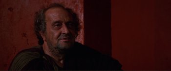 Movie still from “Fellini Satyricon” (1969), directed by Federico Fellini – An older man with a beard and mustache looking at the camera; Close Up shot, Over the shoulder angle