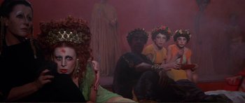Movie still from “Fellini Satyricon” (1969), directed by Federico Fellini – A group of people sitting in a living room; Medium shot, Over the shoulder angle