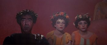Movie still from “Fellini Satyricon” (1969), directed by Federico Fellini – A group of three people with flowers in their hair; Medium shot, High angle