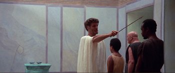Movie still from “Fellini Satyricon” (1969), directed by Federico Fellini – A man in a white robe holding a knife and pointing at a boy; Medium shot, Low angle