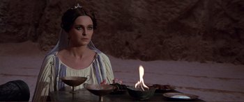 Movie still from “Fellini Satyricon” (1969), directed by Federico Fellini – A woman sitting in front of a table with a lit candle; Medium shot, Over the shoulder angle